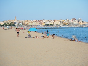 A beach with people sunbathing and swimming, a clear sky, and buildings in the background.