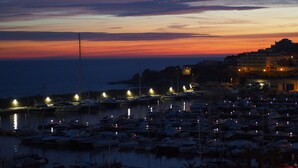 Un puerto deportivo al atardecer con barcos amarrados y un paisaje urbano al fondo.