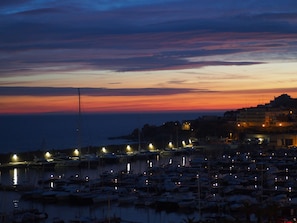 A marina at dusk with boats docked and a cityscape in the background.