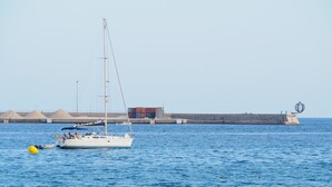 Un velero anclado cerca de un puerto con un faro y una espigada en el fondo.
