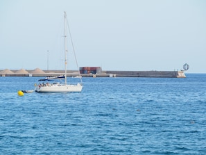 A sailboat anchored near a port with a lighthouse and a breakwater in the background.