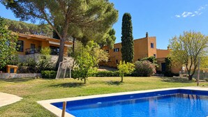 Una piscina con borde de piedra, rodeada por un césped cuidado y diversas especies de árboles.
