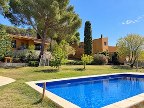 A swimming pool with a stone border, surrounded by a well-maintained lawn and various trees.