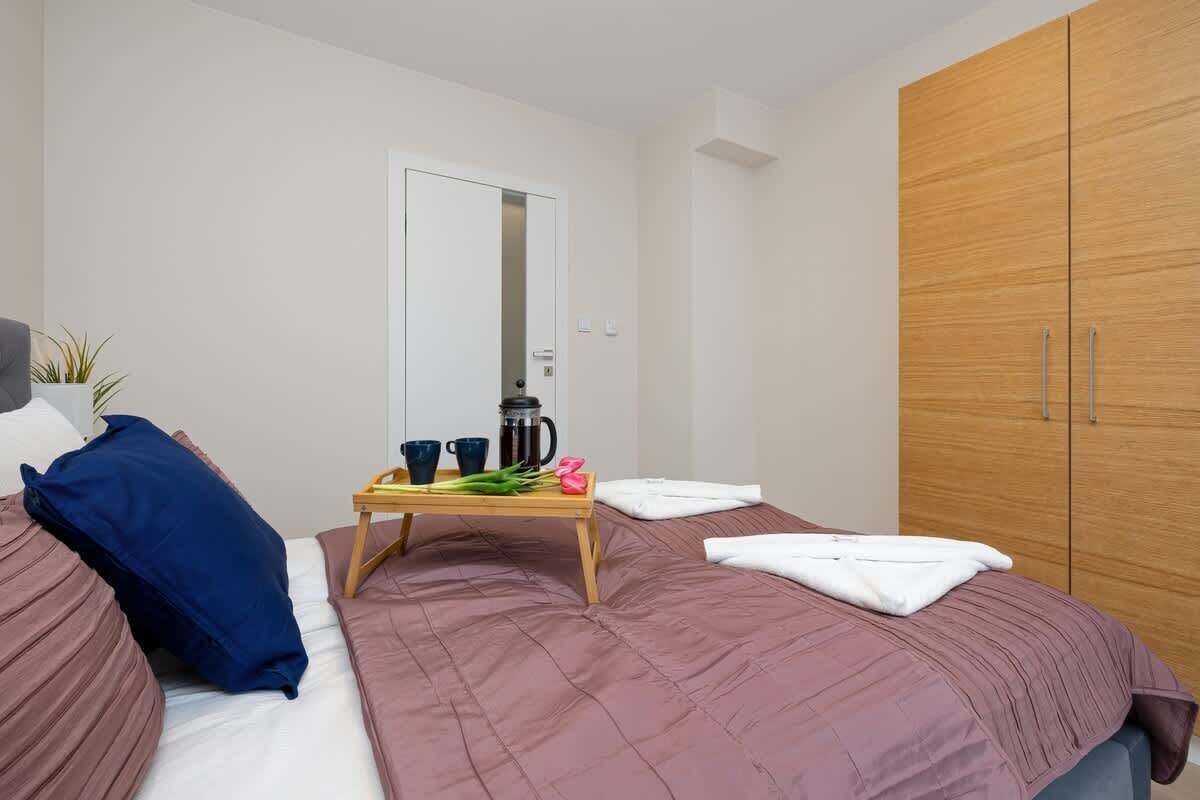 A bedroom with two beds, a wooden wardrobe, a bedside table with a coffee pot, cups, and a plant.