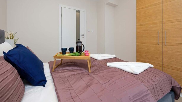 A bedroom with two beds, a wooden wardrobe, a bedside table with a coffee pot, cups, and a plant. - Apartment with Balcony | Pool, Gym, 100 m to the Beach (Rewal)