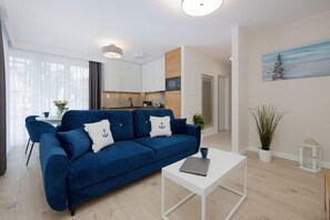 A modern living room with a blue sofa, white coffee table, and a view of the kitchen.