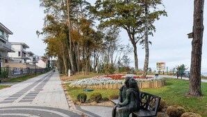 A park with a statue of a woman sitting on a bench, surrounded by trees and flower beds. - Apartment with Balcony | Pool, Gym, 100 m to the Beach (Rewal)