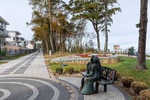 A park with a statue of a woman sitting on a bench, surrounded by trees and flower beds.