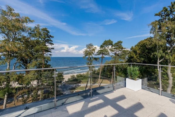 A balcony with a clear view of the sea and beach, surrounded by trees.