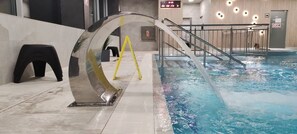 An indoor swimming pool with a clear water feature, a metal railing, and a yellow safety sign.