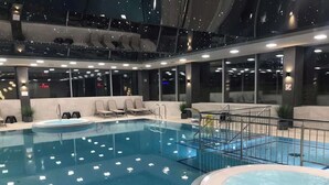 An indoor swimming pool with a hot tub, seating area, and a view of the night sky through the ceiling. - Apartment with Balcony | Pool, Gym, 100 m to the Beach (Rewal)