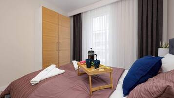 Ein Hotelzimmer mit einem Bett, einem Nachttisch aus Holz mit einem Tablett mit Frühstücksangeboten, einer Kaffeemaschine und einem großen Fenster mit Vorhängen.