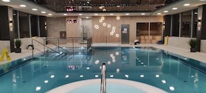 Una piscina interior con una plataforma de salto central, rodeada por un diseño arquitectónico moderno que incluye iluminación empotrada y un revestimiento de madera.