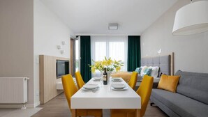A modern living room with a dining table set for four, a grey sofa, and a TV on the left.