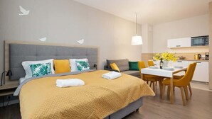 A modern hotel room with a large bed, a dining area, and a kitchenette.