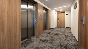 A hallway with wooden paneling, a carpeted floor, and two elevators.