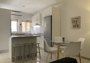 Eine kompakte Küche mit einer zentralen Kochinsel, Barhocker, einem Esstisch mit Stühlen, einem Kühlschrank und einem Bild an der Wand.