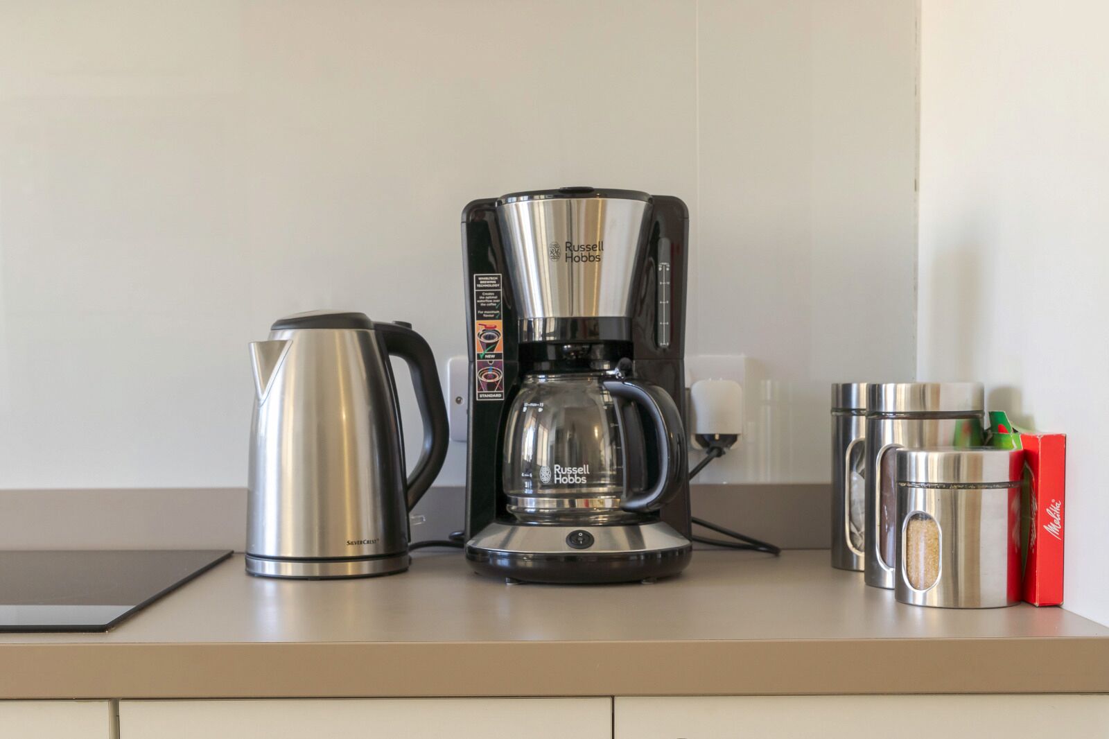 Una cocina con cafetera, hervidor y taza sobre la encimera.