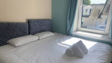 Ein ordentlich bezogenes Bett mit weißen Bettwäsche und Kissen, ein Fenster mit Vorhängen und ein Blick auf Gebäude im Freien.