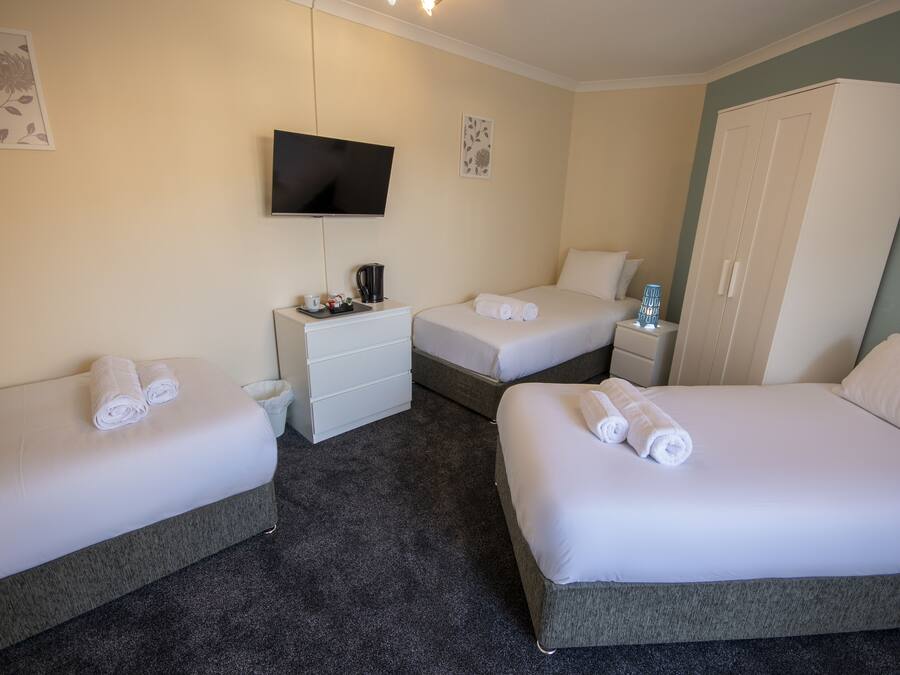 A hotel room with two single beds, a TV mounted on the wall, a wardrobe, and a small bedside table with a lamp.