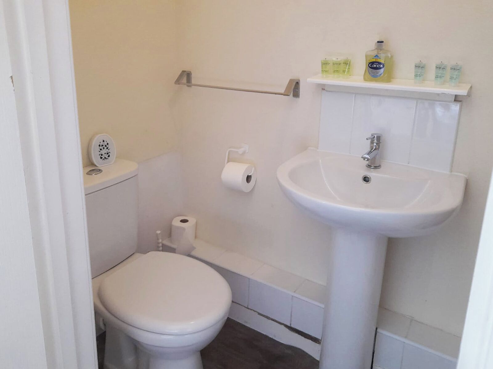 A small, clean bathroom with a toilet, a sink, and a shelf with toiletries.
