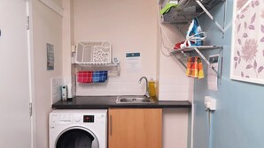 A compact kitchen with a washing machine, a sink, and a drying rack. - Irvine Riverside Guesthouse (Irvine)