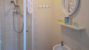 A bathroom with a shower, a sink, a mirror, and a shelf with toiletries. - Irvine Riverside Guesthouse (Irvine)
