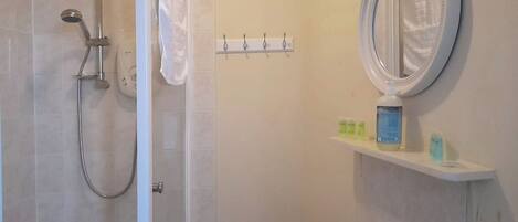 A bathroom with a shower, a sink, a mirror, and a shelf with toiletries.