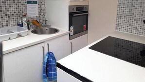 A kitchen with a sink, stove, oven, and a microwave. There are cleaning supplies on the counter. - Irvine Riverside Guesthouse (Irvine)