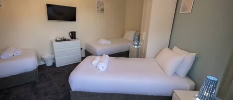 A hotel room with a large bed, two smaller beds, a TV, a wardrobe, and a nightstand with a lamp.