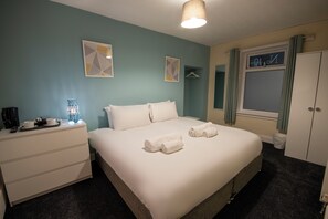 A neatly made bed with towels, a bedside table with a lamp, and a wardrobe. - Irvine Riverside Guesthouse (Irvine)
