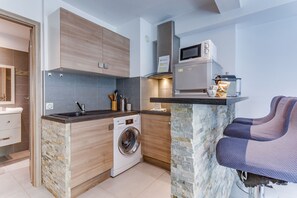 Cocina compacta con lavadora integrada, microondas y una pequeña zona de estar con banco.