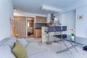 A modern living room with a glass coffee table, a sofa, and a kitchen area in the background. - SUEDE 2 AP4208 By Riviera Holiday Homes (Niza)