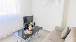 En moderne stue med et glasbord, et fladskærms-TV, en beige sofa og en potteplante.