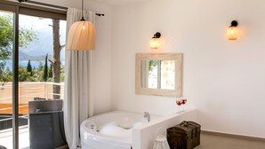 A modern bathroom with a bathtub, a large window with a view of the outdoors, and a wooden chest of drawers. - Kale Suites (Kas)