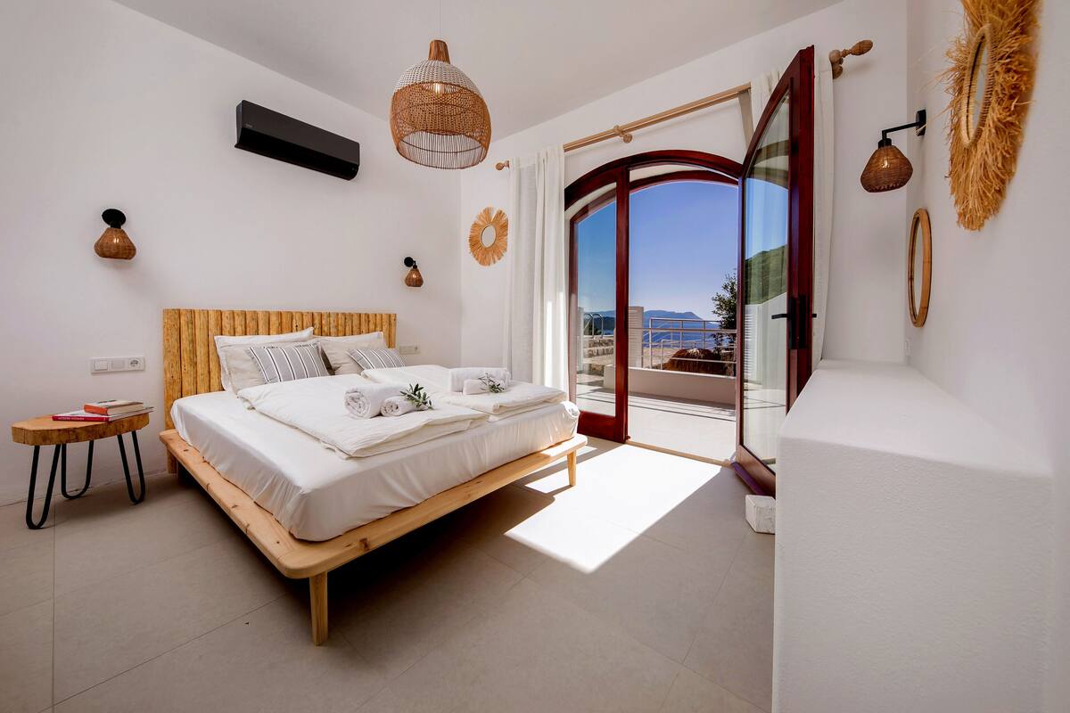 A bedroom with a wooden bed, a small bedside table, a large window with a view, and a ceiling fan.