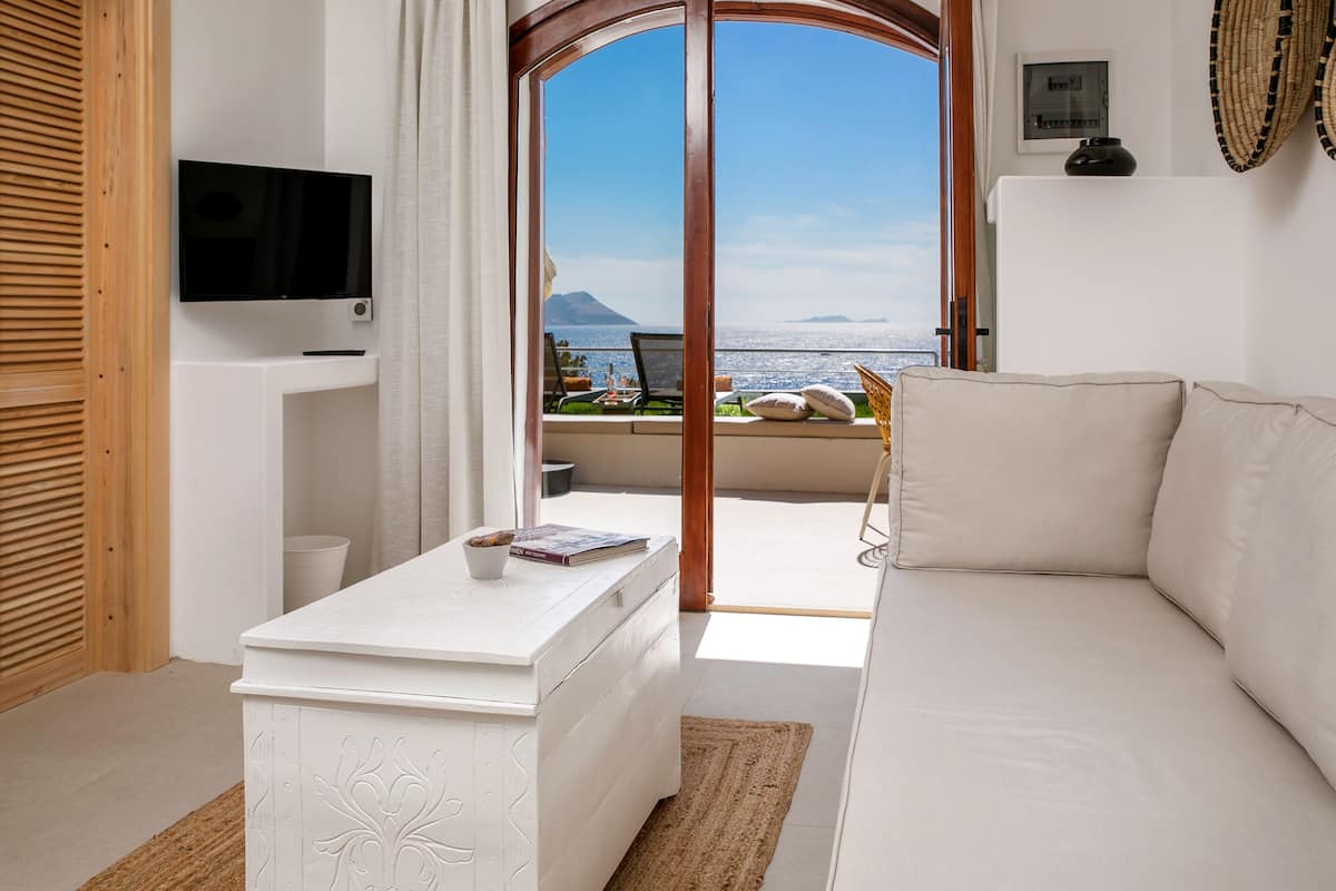 A modern living room with a white sofa, a flat-screen TV, and a view of the sea.