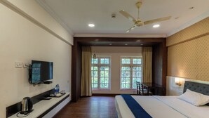 Quarto de hotel com cama, televisão, escrivaninha e janela com cortinas.