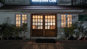 Exterior do Malayalee Club, com uma placa sobre a entrada, plantas em vasos e calçada de azulejos.