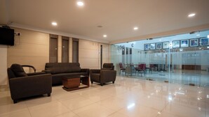 Um lobby de hotel moderno com um conjunto de sofás, uma mesa de centro e um painel de vidro separando a área de estar da sala de jantar.