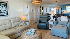Uma sala de estar com sofá, poltronas, mesa de centro e um espaço de jantar com cadeiras e mesa.