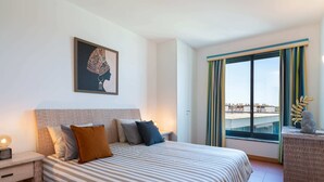 Une chambre d’hôtel avec un grand lit, une table de chevet, une œuvre d’art encadrée au mur, une fenêtre avec des rideaux et une vue sur les bâtiments à l’extérieur.