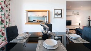 Un coin repas avec une table moderne dressée pour deux personnes, une sculpture métallique décorative en guise de centre de table et une vue sur la cuisine.