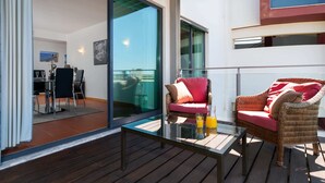 Un balcon agrémenté de meubles en osier, d’une table en verre et d’un coin repas avec des chaises et une table.