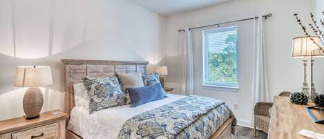 A bedroom with a wooden bed, patterned bedding, a nightstand with a lamp, a wooden dresser, and a ceiling fan.