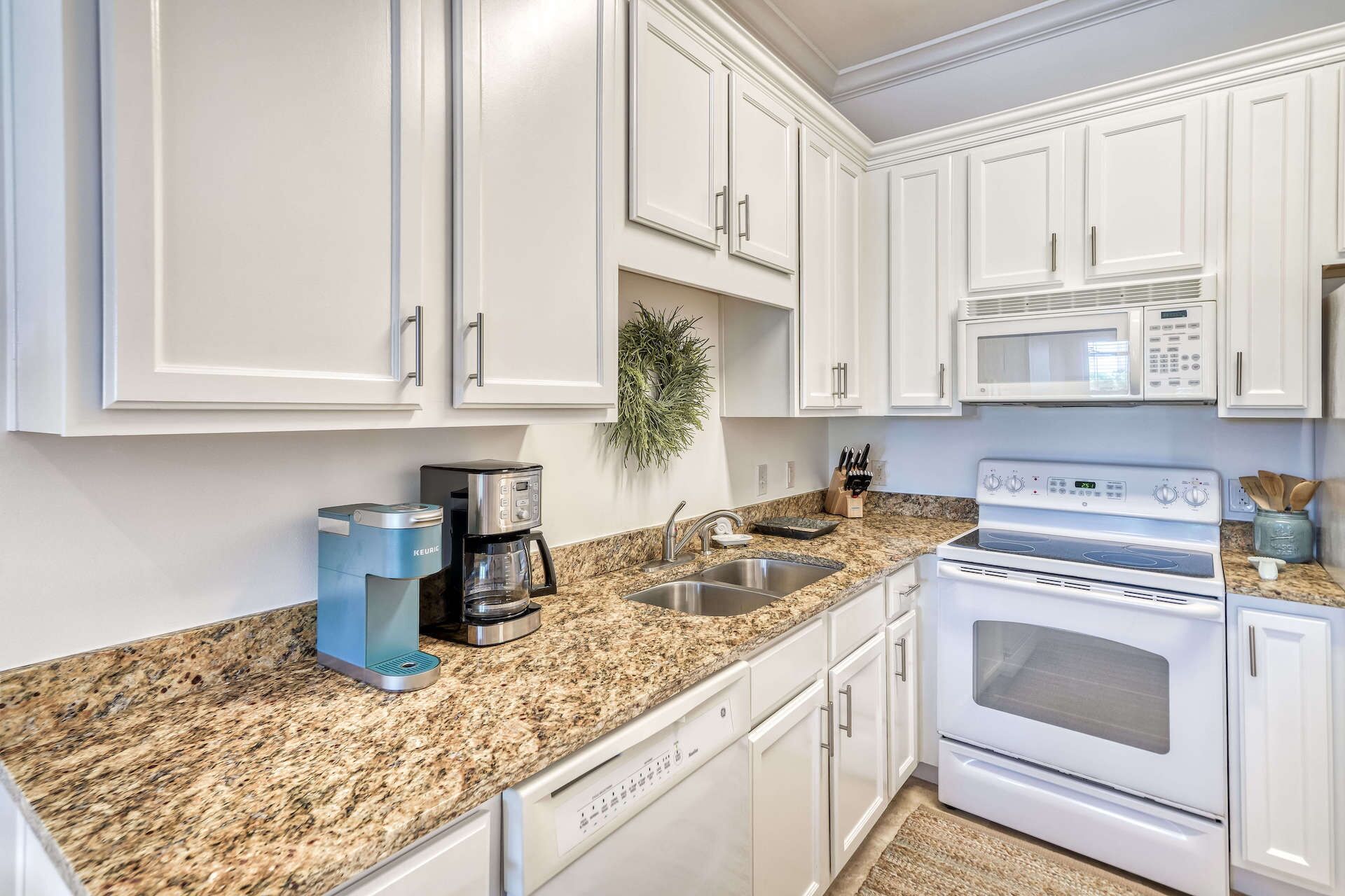 A kitchen with white cabinets, a granite countertop, a Keurig coffee maker, a microwave, and a stove.