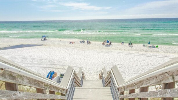 A beach with a wooden staircase leading down to the sand, a few umbrellas, and people relaxing.
