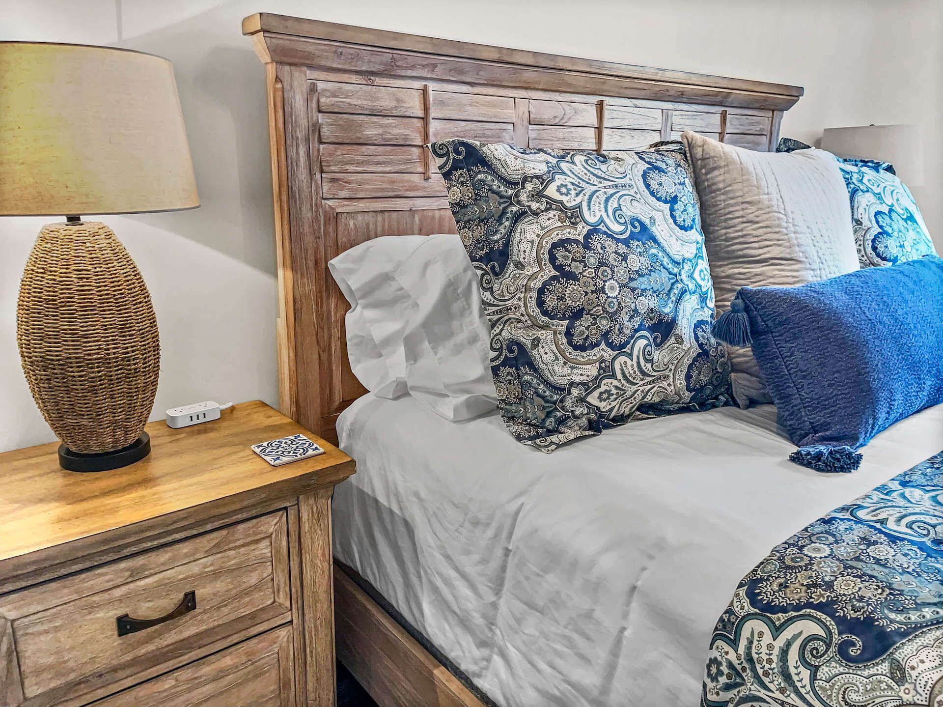 A neatly made bed with patterned pillows, a bedside lamp, and a wooden nightstand with a drawer.