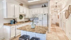 A kitchen with white cabinets, granite countertops, a central island with stools, a refrigerator, and a chandelier.