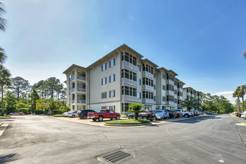 A multi-story hotel with a parking lot, several cars, and palm trees.